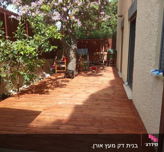 דק עץ בגינה עם עץ פורח ורהיטי גן